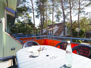 Une table recouverte d’une nappe blanche, une bouteille d’eau et un menu, le tout sur un balcon doté de balustrades et de chaises rouges.
