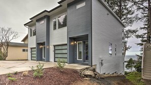 Une maison moderne à deux étages, dotée d’un garage, d’un patio couvert et offrant une vue sur l’océan.