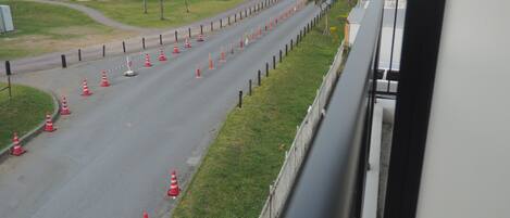 A road lined with traffic cones and a fence, with a grassy area and a building in the background.