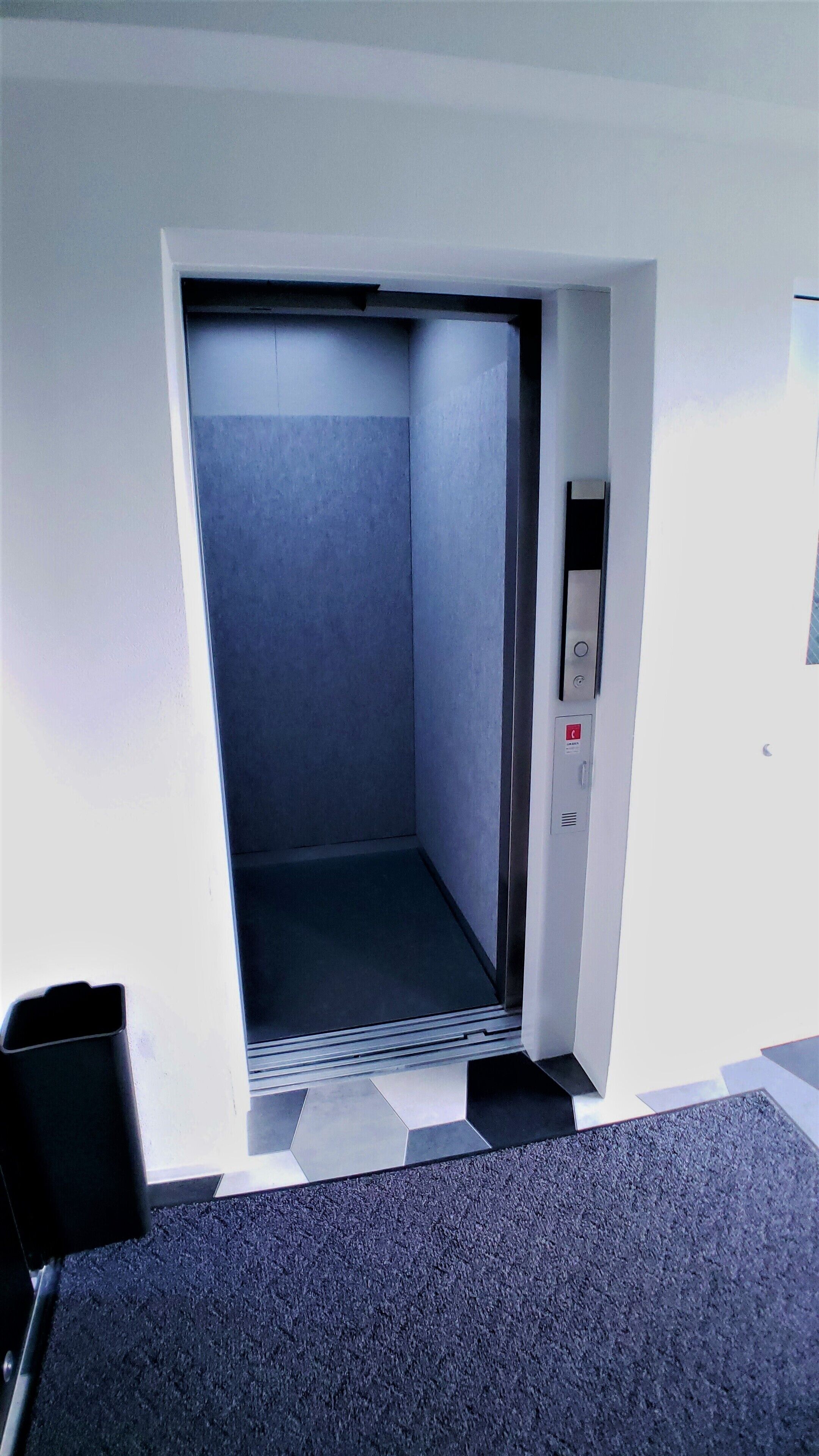 An elevator with a metallic control panel and a grey interior.