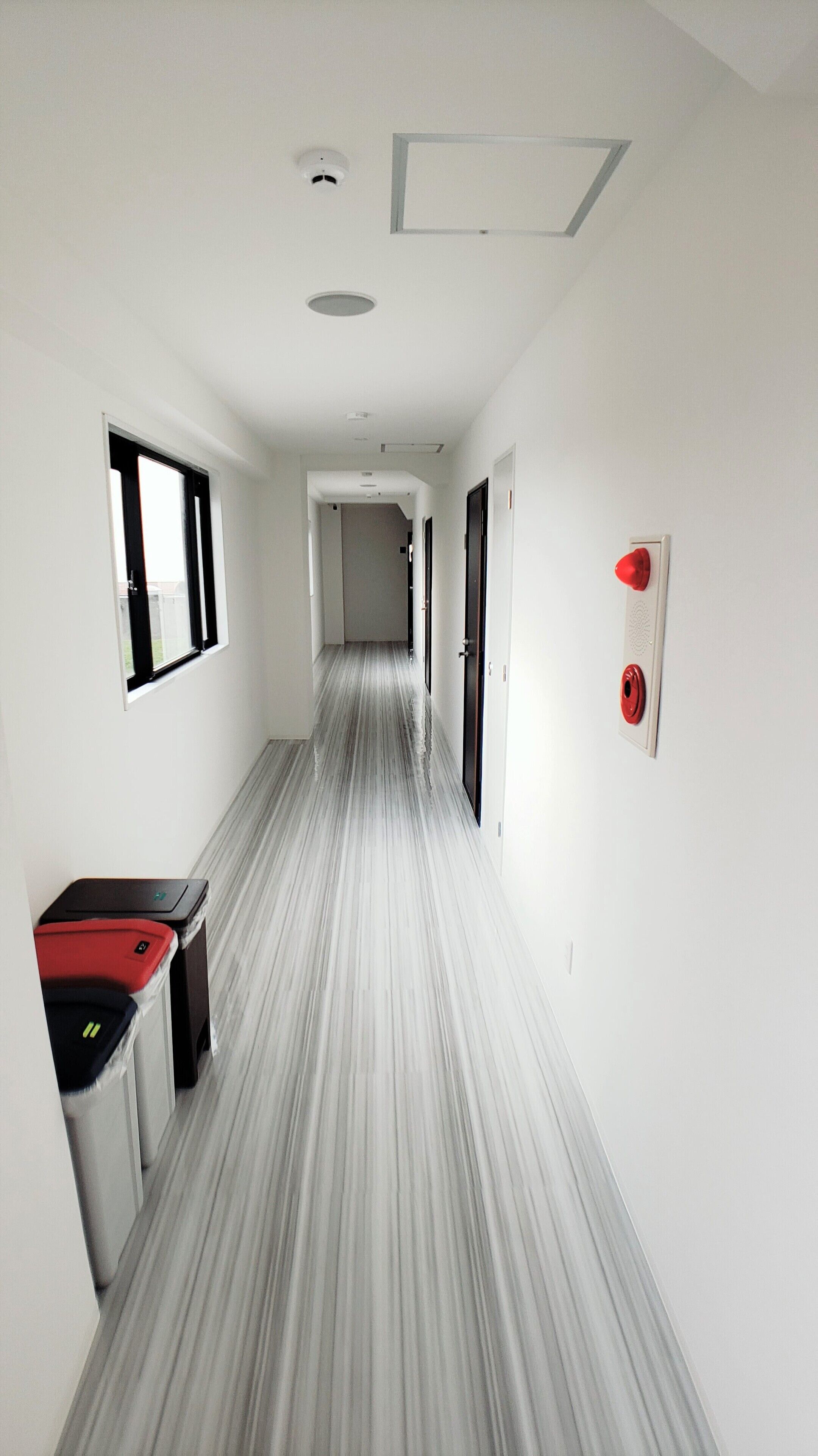 A narrow hallway with a striped floor, white walls, and a door at the end.