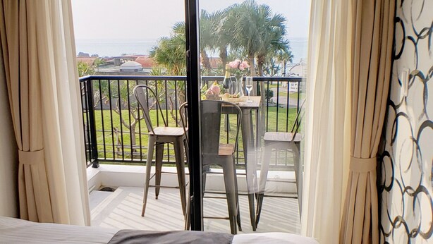 A hotel room with a bed, a balcony with a table and chairs, and a view of the outdoors. - Ocean View Araha 305 (Chatan)