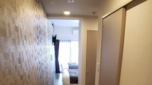 A hallway with a patterned wall, wooden flooring, and a bed in the background. - Ocean View Araha 305 (Chatan)