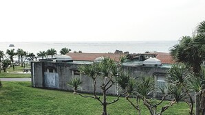 A grassy area with trees, a concrete building, and a view of the sea. - Ocean View Araha 305 (Chatan)