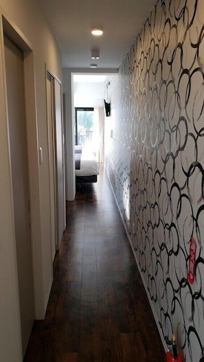 A hallway with a patterned wall, a bed in the background, and a fire extinguisher on the wall.