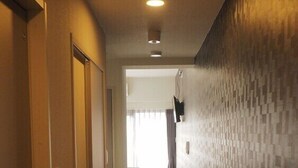 Un pasillo con piso de madera, un muro de azulejos y una cama a lo lejos.