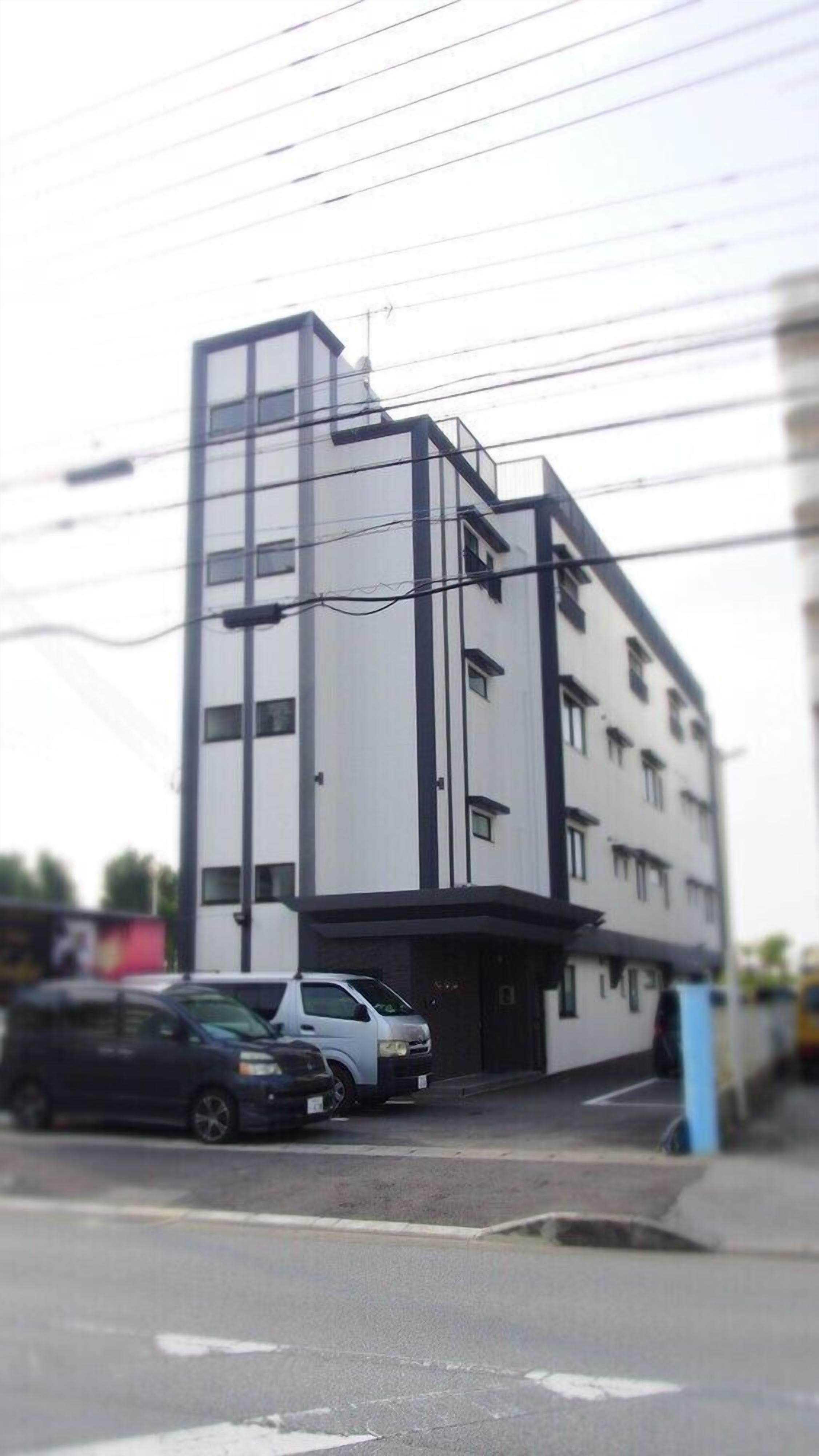 Ein modernes Gebäude mit weißer Fassade und schwarzen Akzenten, mit mehreren Stockwerken und einem flachen Dach.