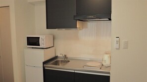 Una cocina compacta con microondas, lavamanos y un refrigerador pequeño.
