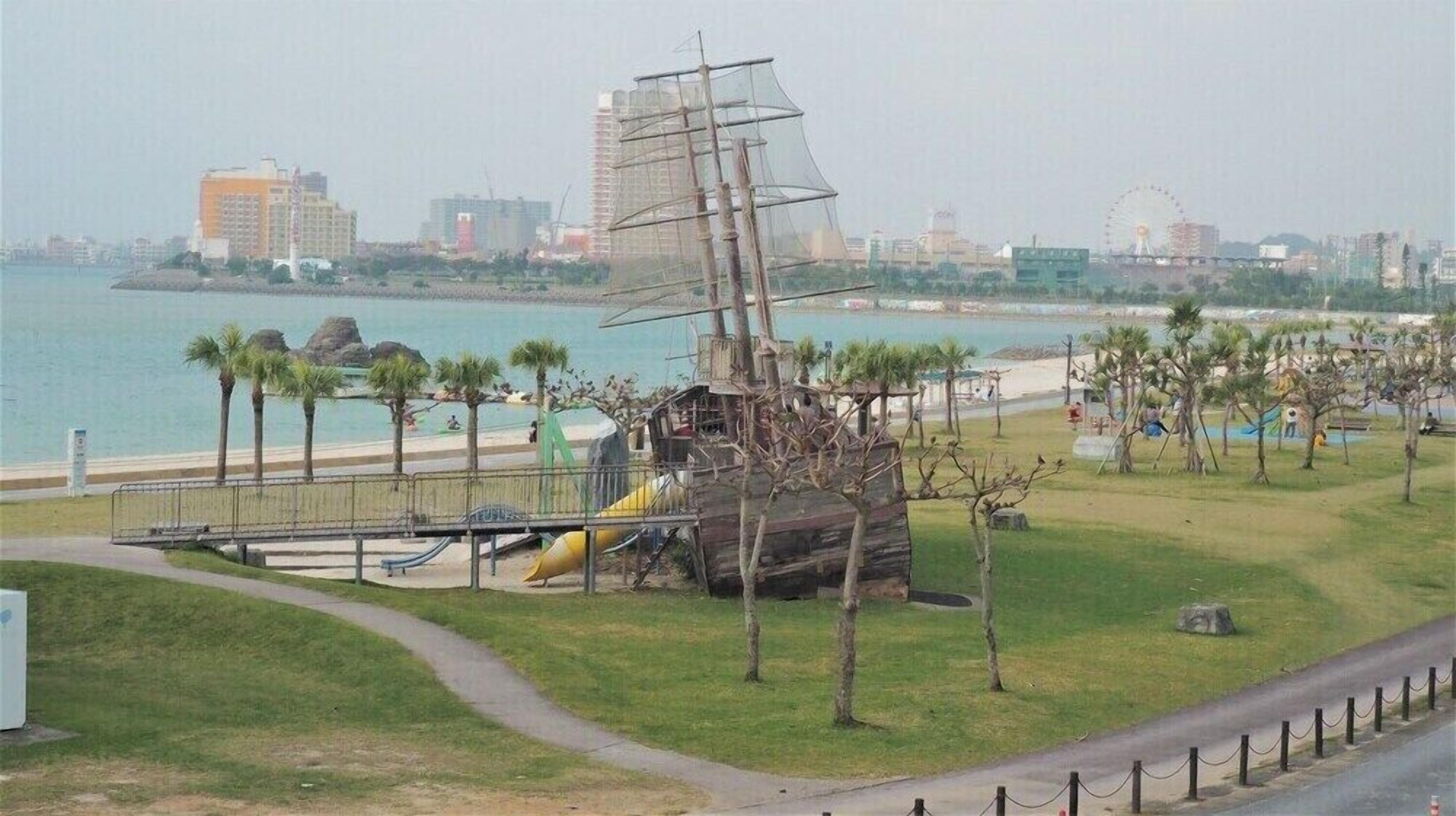A park with a shipwreck sculpture, a playground, and a view of the city skyline and water.