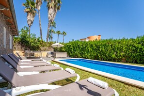Área de piscina com espreguiçadeiras e mesa, cercada por vegetação e palmeiras.