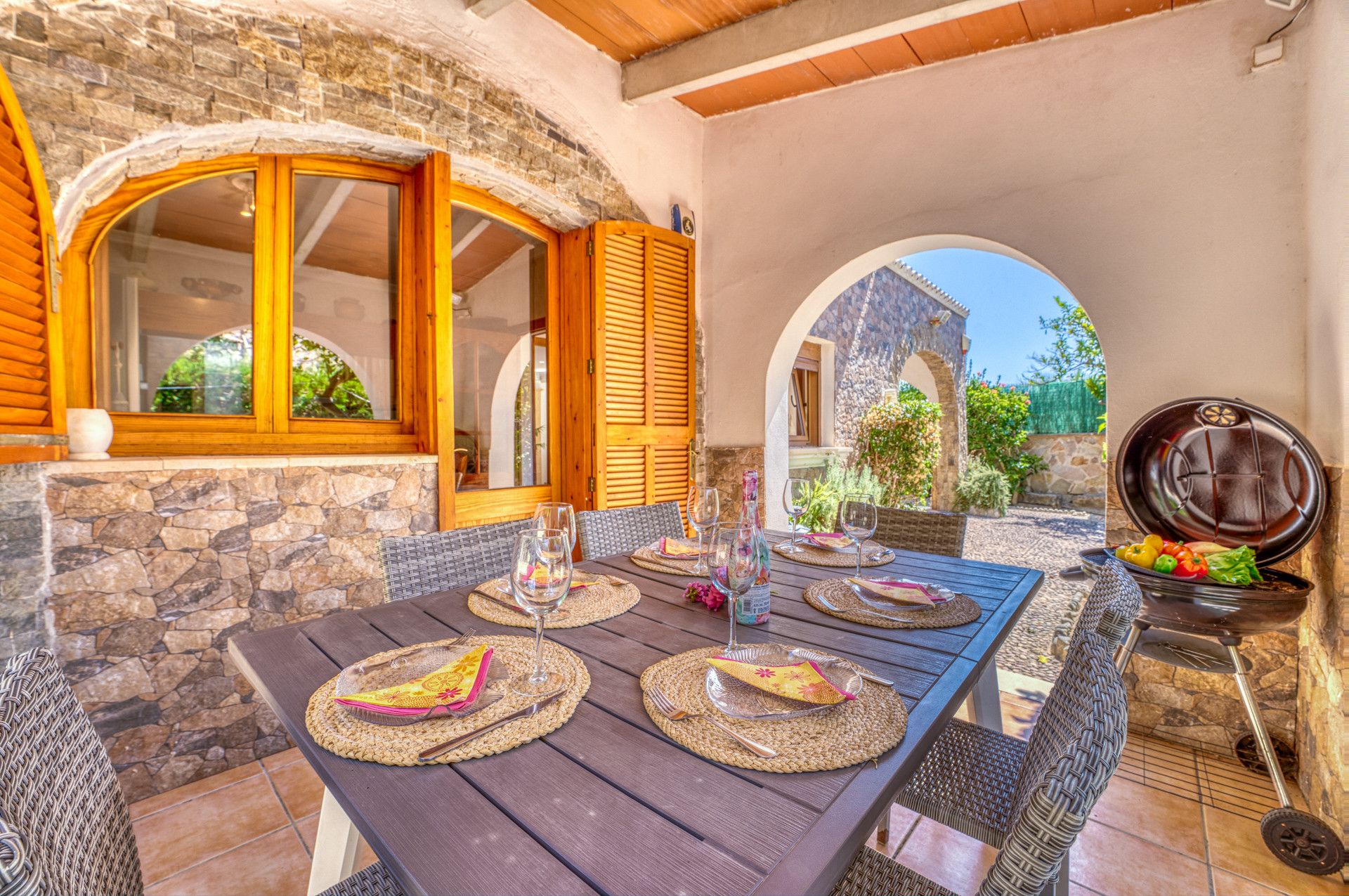 An outdoor dining area with a stone wall, wooden shutters, and a grill station.