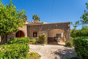 Una casa de piedra con un patio, una zona de estar cubierta al aire libre y un camino de entrada de grava.