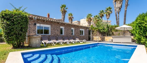 A swimming pool with lounge chairs, a stone building, and palm trees.