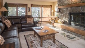 A cozy living room with a leather sofa, a wooden coffee table, and a stone fireplace. - Community Sauna | Mountain Views (Big Sky)