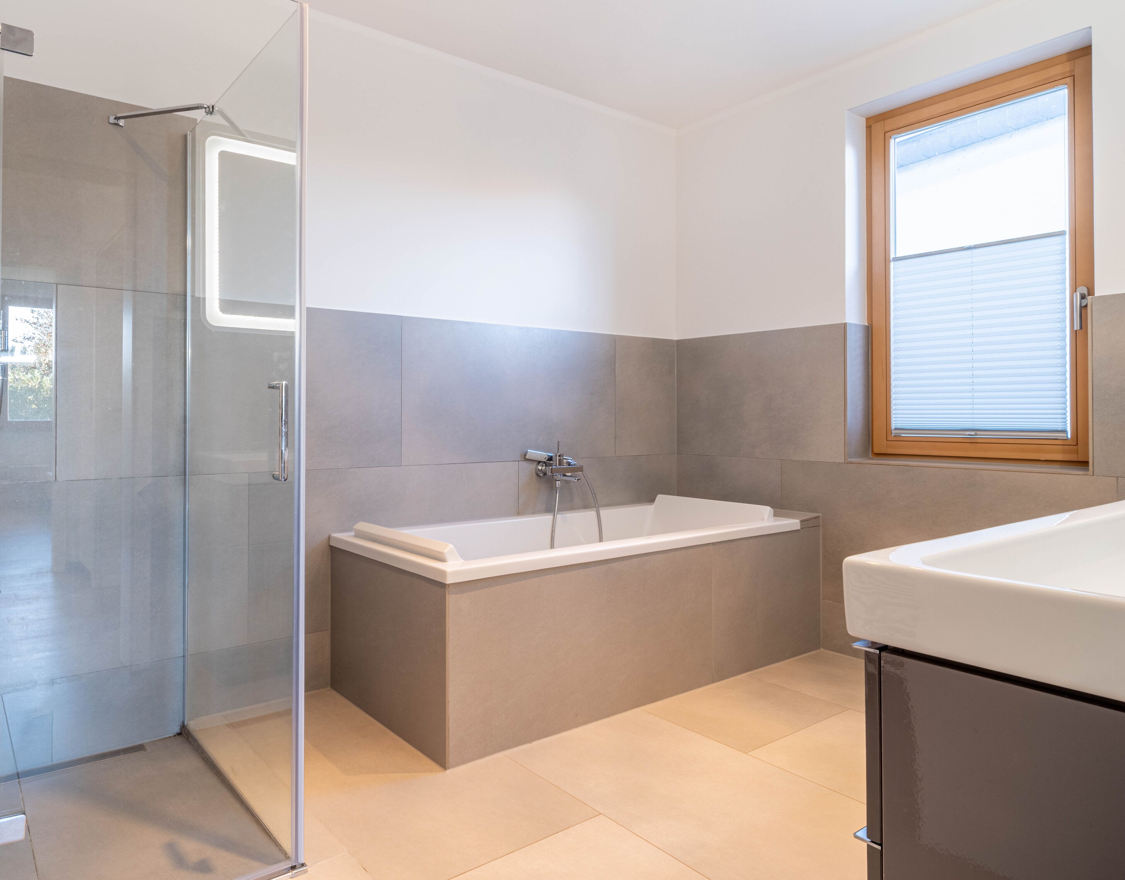 Een moderne badkamer met een inloopdouche, een vrijstaand bad en een raam met zonwering.