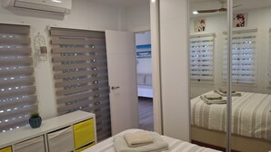 A hotel room with a bed, a bedside table, a mirror, and a window with blinds. - Apartment in El Alamillo (Puerto de Mazarrón)