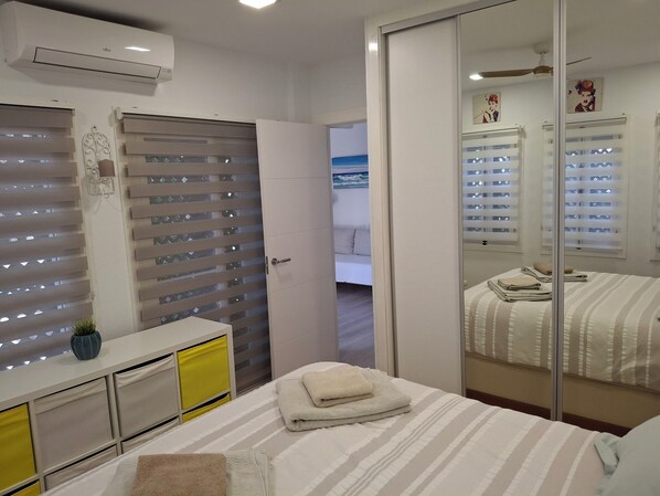 A hotel room with a bed, a bedside table, a mirror, and a window with blinds. - Apartment in El Alamillo (Puerto de Mazarrón)