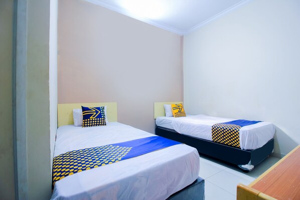 Dos camas individuales con ropa de cama blanca y azul, un banco de madera y una pared lisa.