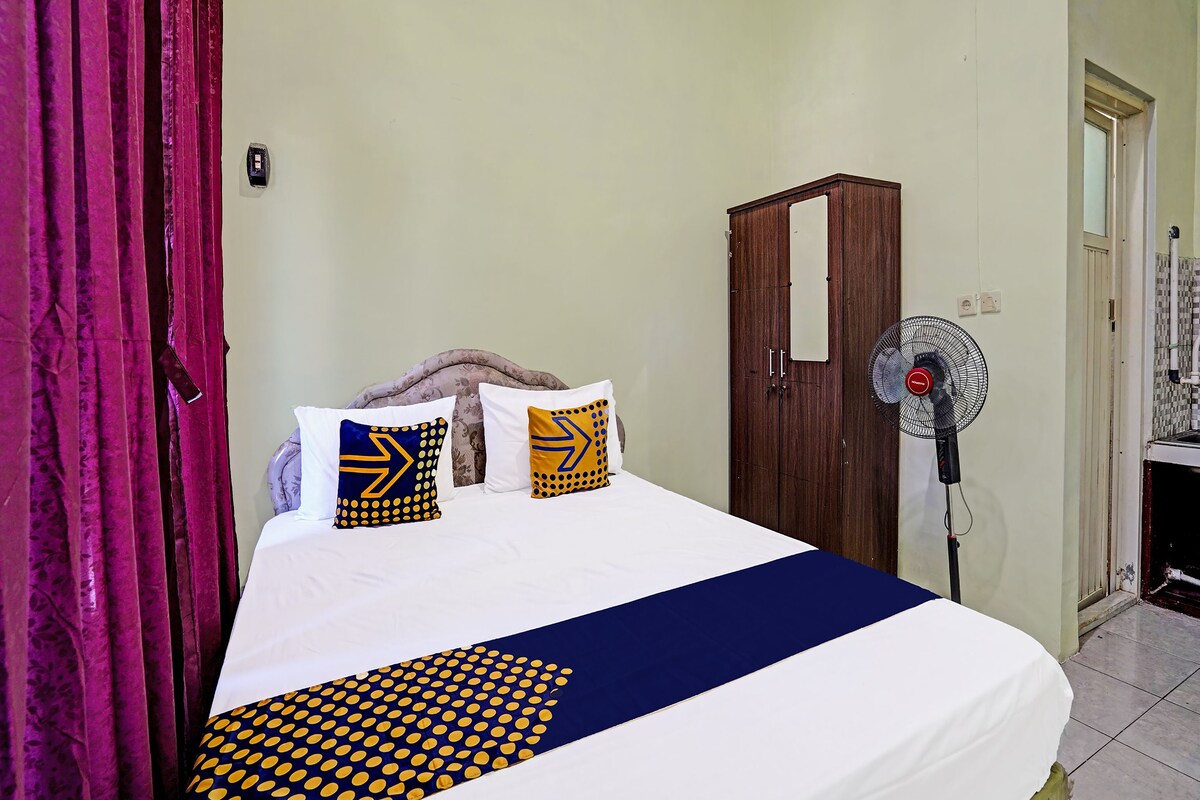 Une chambre d’hôtel avec un lit, une armoire, un ventilateur sur pied et un rideau.