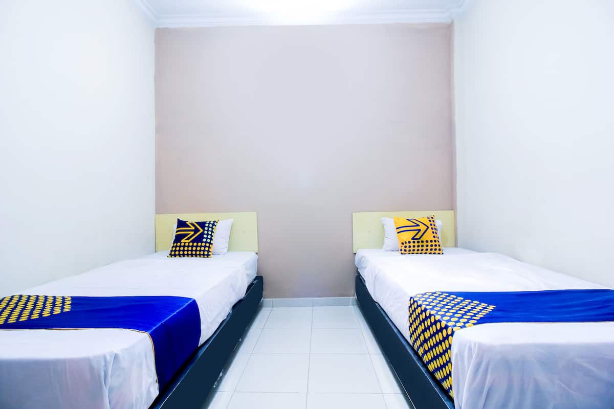 A room with two single beds, each with a blue bedspread and matching pillows, against a plain wall.