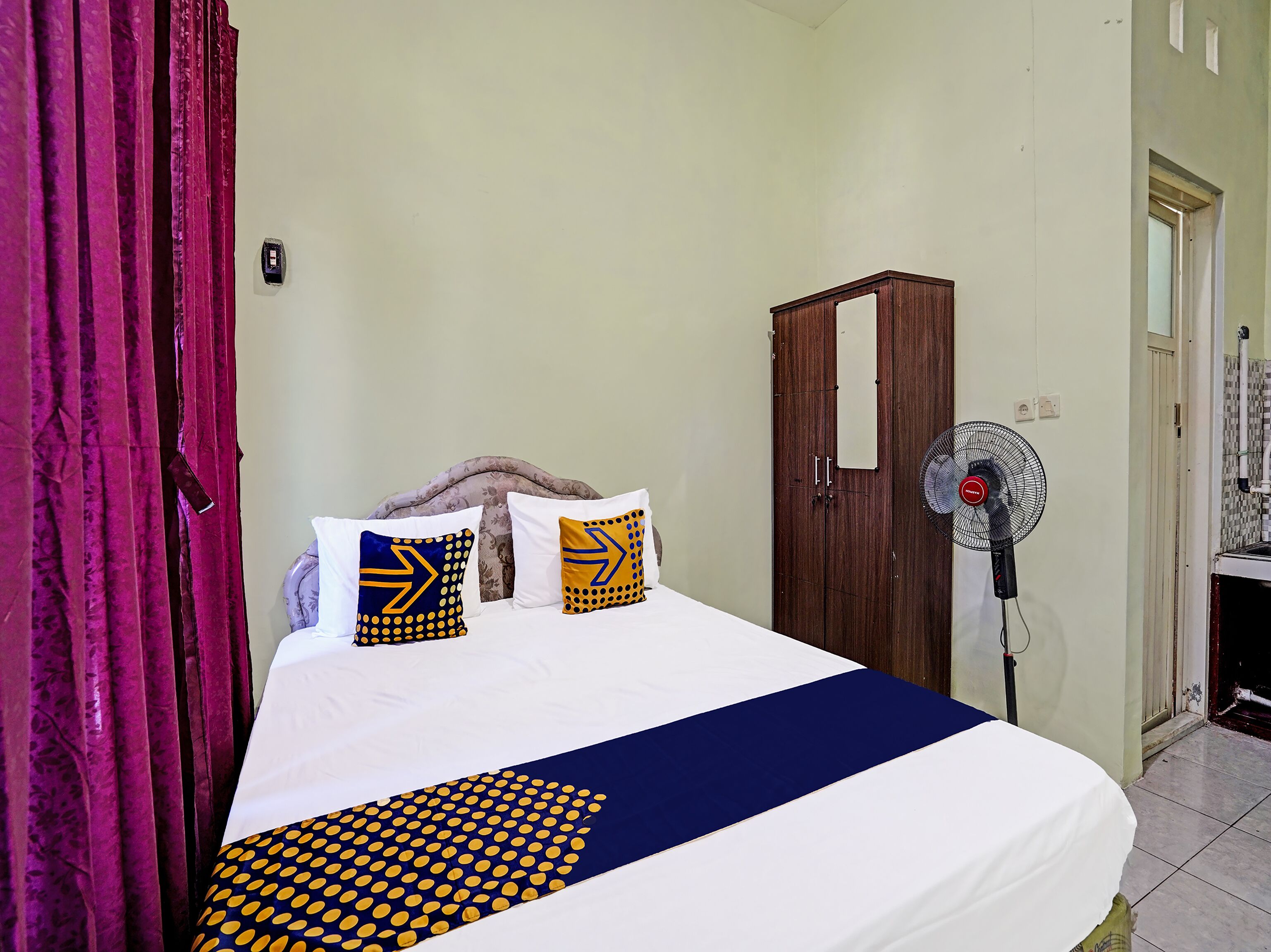 Een hotelkamer met een bed, een kledingkast, een ventilator en een gordijn.