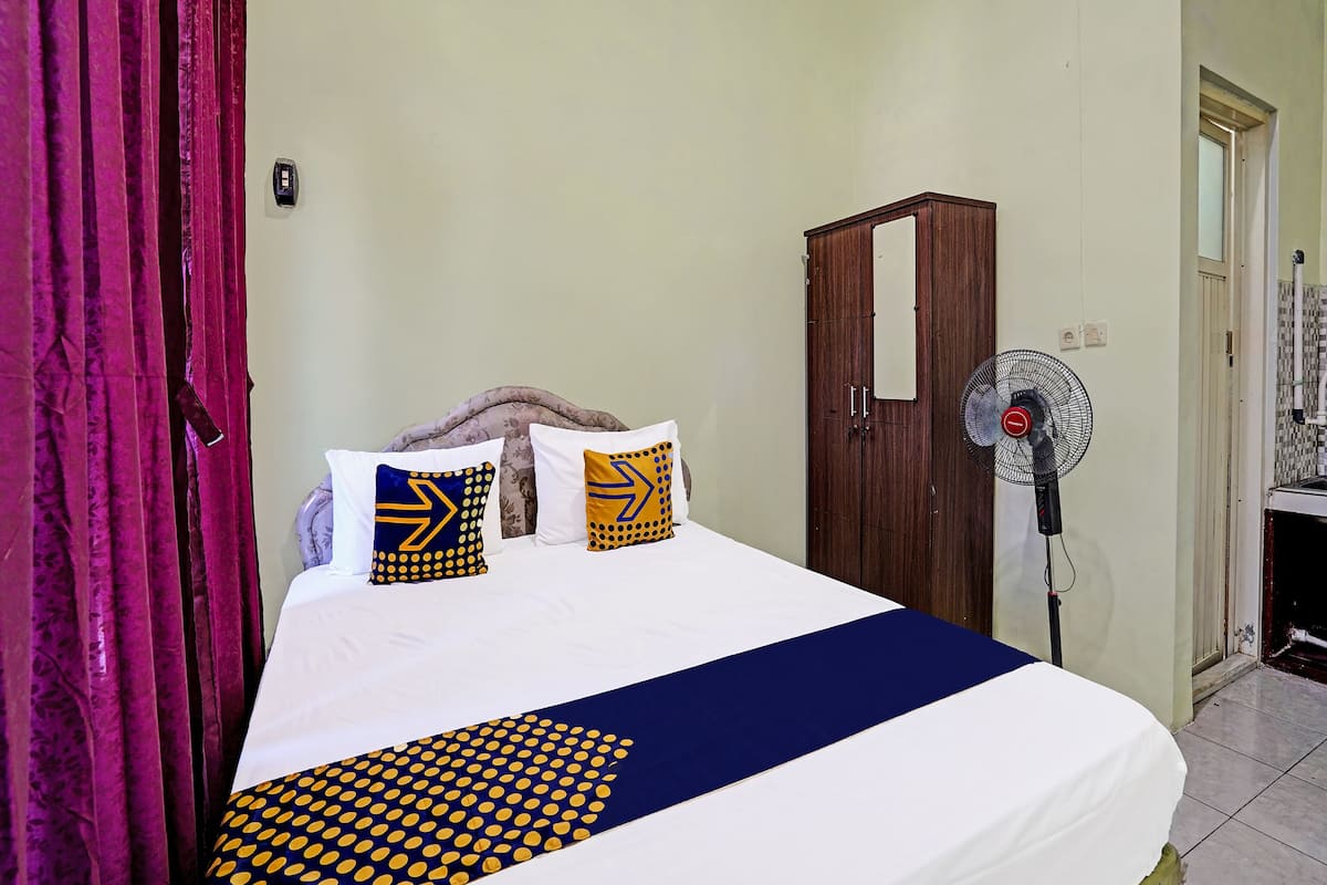 A hotel room with a bed, a wardrobe, a standing fan, and a curtain.