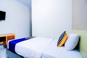 En säng med en vit och blå sängkappa, ett träbord med en låda och en tv som är monterad på väggen.