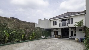 Een gebouw met twee verdiepingen, een balkon, een overdekte ingang en een binnentuin met beplanting.