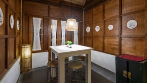 A wooden-paneled room with a white table, three stools, a hanging lamp, and a small plant. - Hotel O Putroyono Homestay (Borobudur)