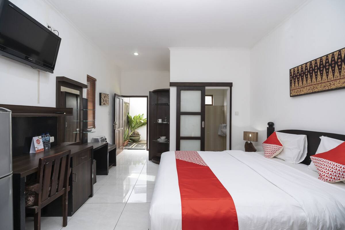 A hotel room with a bed, a desk, a TV, and a door leading to a balcony.