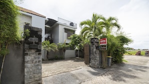 A gated residential property with a white exterior, stone walls, and a tiled driveway. - Hotel O Panen House (Denpasar)