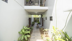 A narrow, covered outdoor corridor with a staircase leading to a balcony, surrounded by potted plants and a small seating area. - Hotel O Panen House (Denpasar)