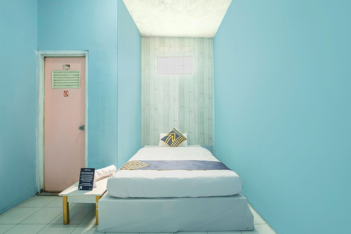 Una habitación pequeña y ordenada, con cama, mesa y puerta.