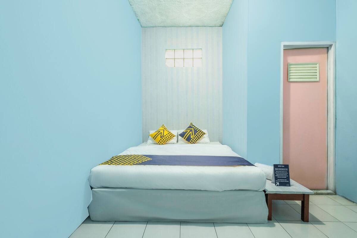 A neatly arranged bedroom with a bed, pillows, a bedside table, and a sign.