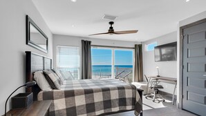 A modern hotel room with a large bed, a desk, a ceiling fan, and a view of the ocean.