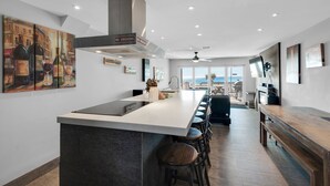 A modern kitchen with a central island, bar stools, and a view to the outside.
