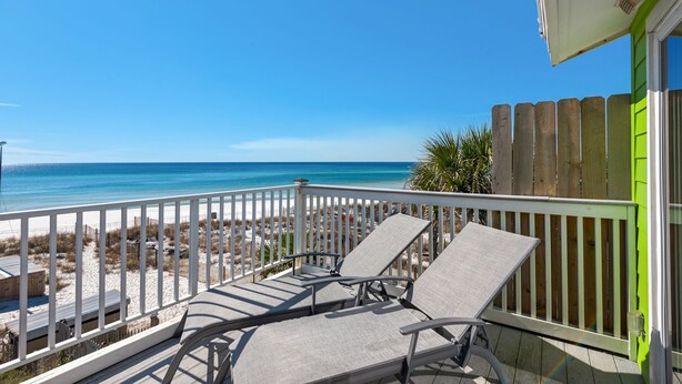 A balcony with two lounge chairs, a white railing, and a view of the beach and ocean.