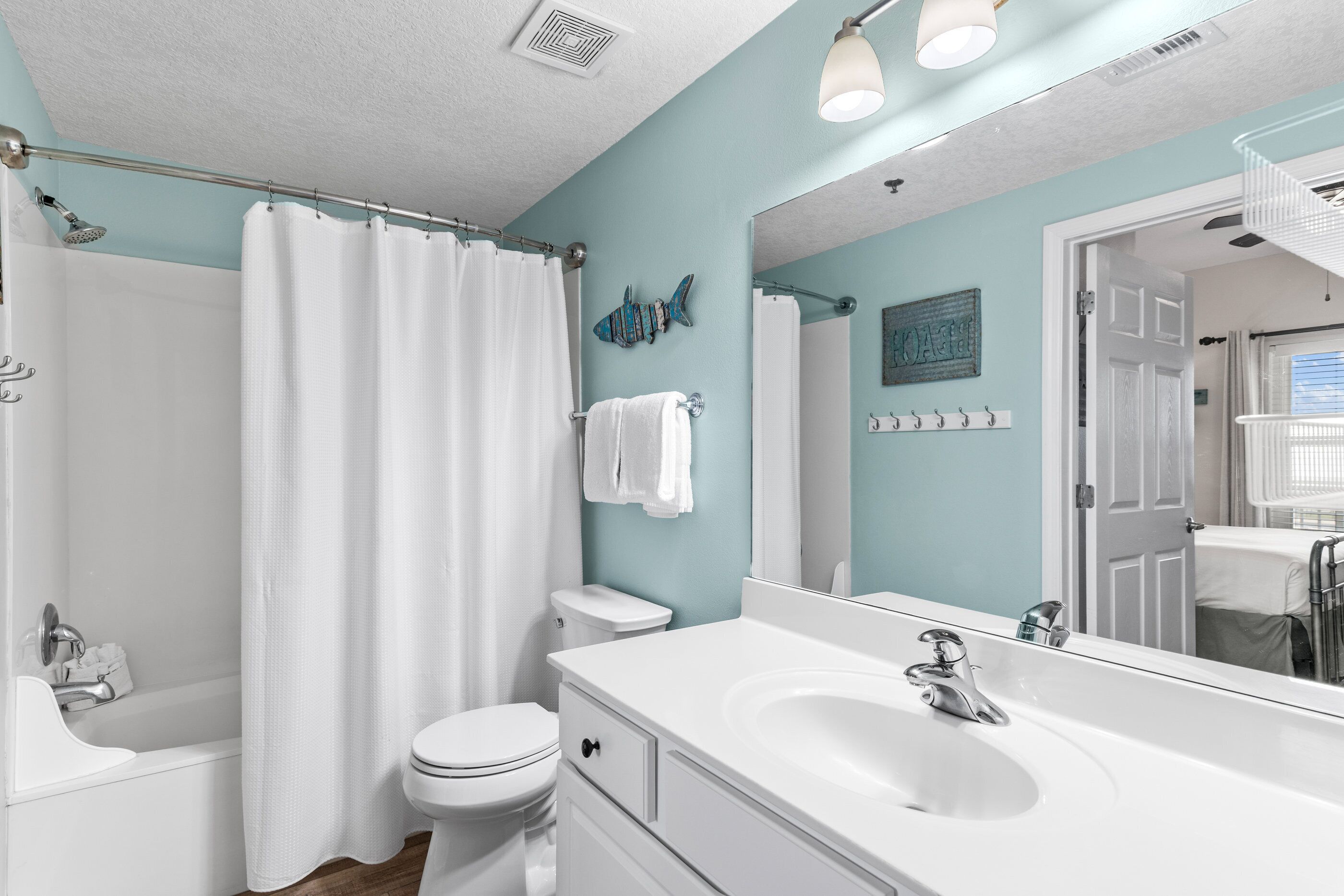 Un baño con un lavamanos blanco, un inodoro, una ducha con cortina blanca y un espejo con lámpara.