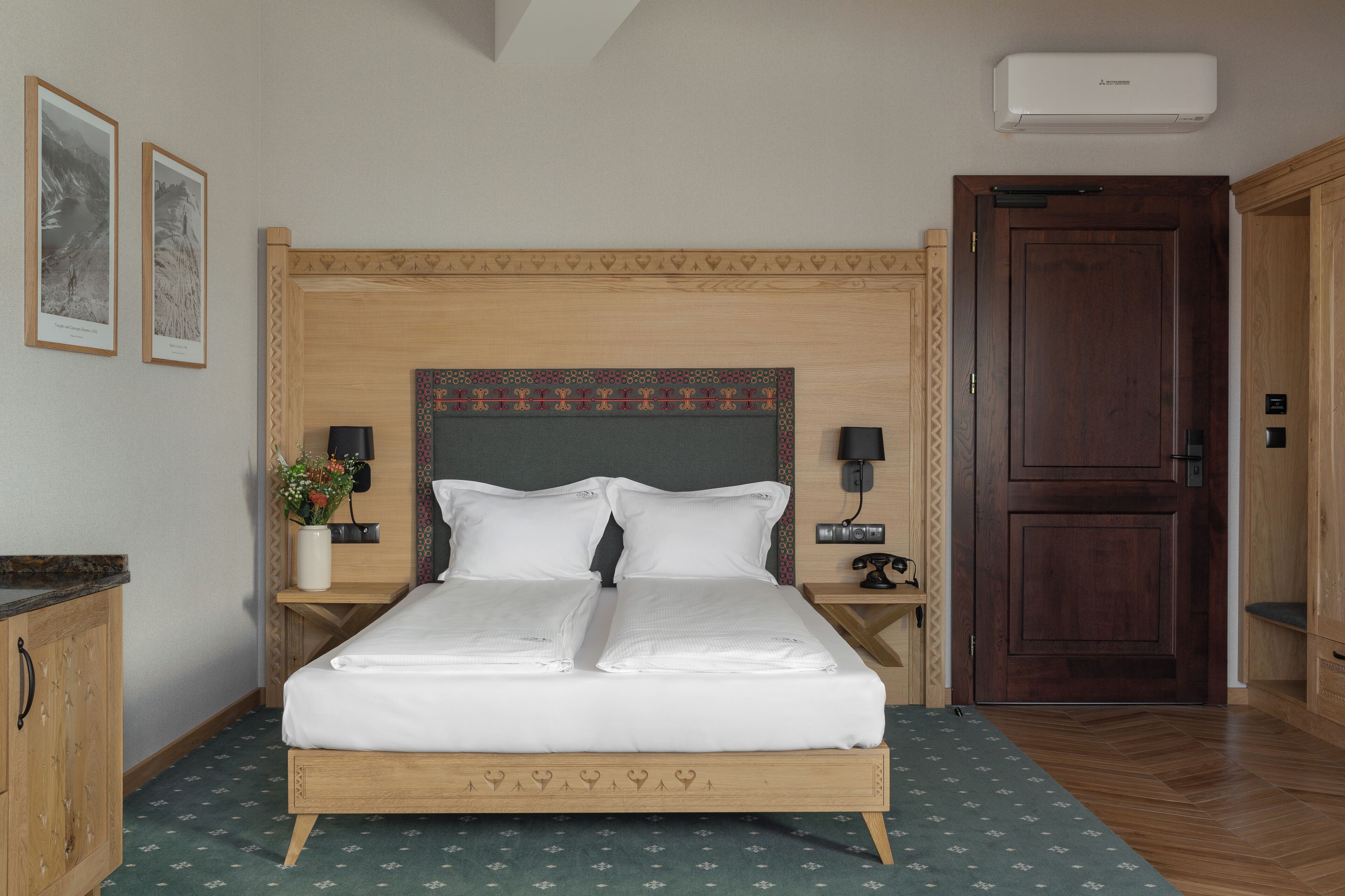 Un lit bien fait, avec du linge de lit blanc, une tête de lit en bois, une table de chevet avec une lampe et un climatiseur fixé au mur.