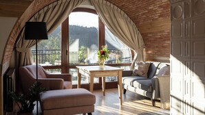 A cozy living room with a brick ceiling, a large window with curtains, a sofa, a chair, a table, and a potted plant. - Aparthotel Cristina (Zakopane)