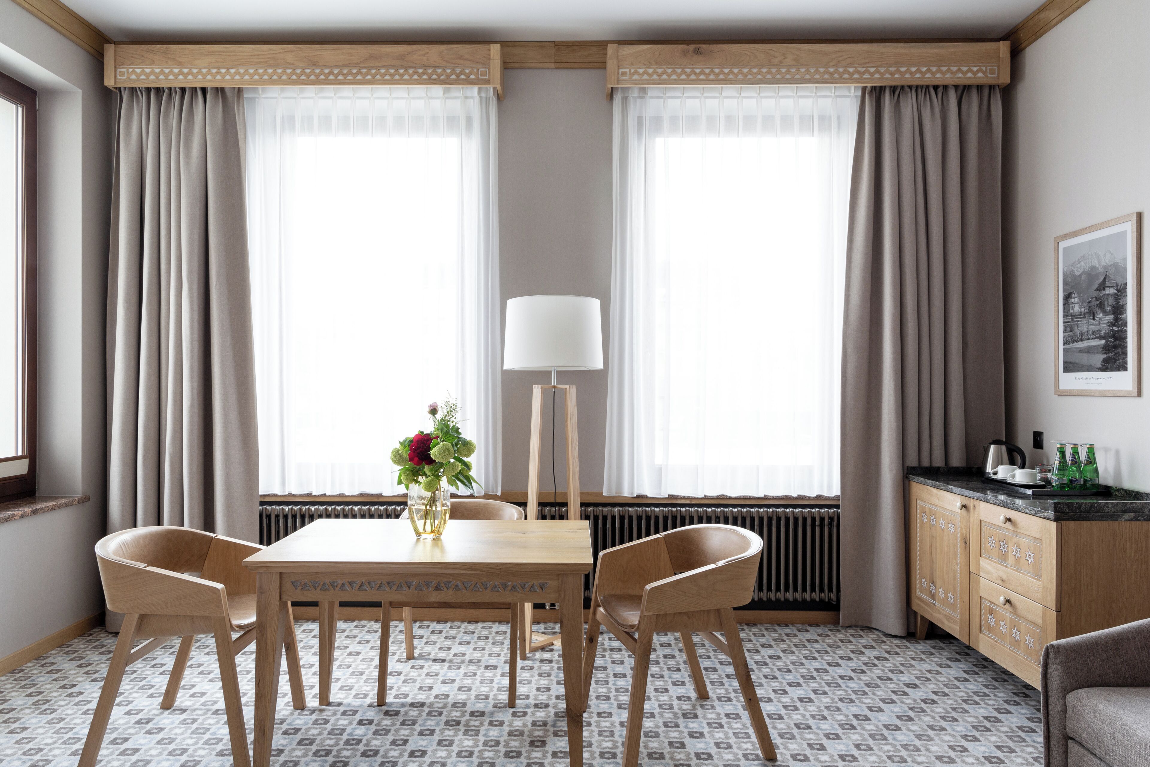 A room with a wooden table and chairs, a floor lamp, a radiator, and a window with curtains.
