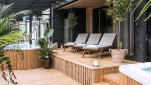A modern outdoor lounge area with wooden decking, lounge chairs, and a hot tub. - Aparthotel Cristina (Zakopane)