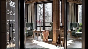 A room with a large window, a wooden chair, a table, and a sofa. - Aparthotel Cristina (Zakopane)