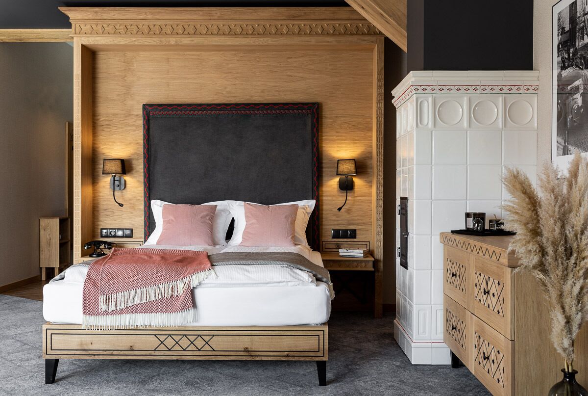 Un dormitorio con cabecera de madera, dos lámparas de noche, una mesita de noche, un aparador de madera y un jarrón decorativo.