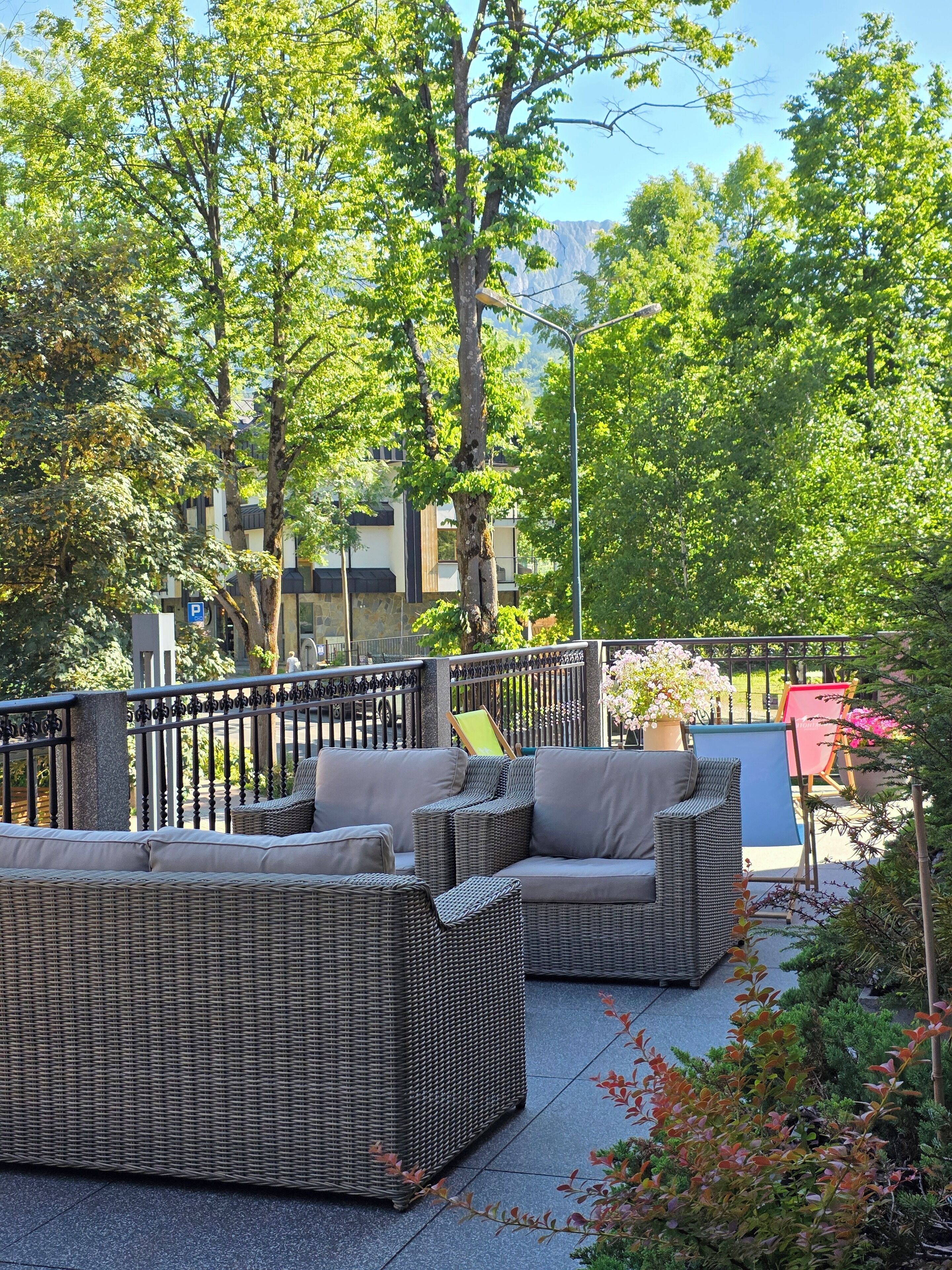 Outdoor wicker furniture, a metal fence, and a view of buildings in the background.