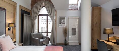 A hotel room with a bed, a desk, a chair, a TV, a window with curtains, and a view of buildings outside.