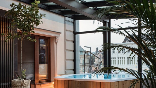 A modern spa area with a hot tub, wooden deck, and large windows offering city views. - Aparthotel Cristina (Zakopane)