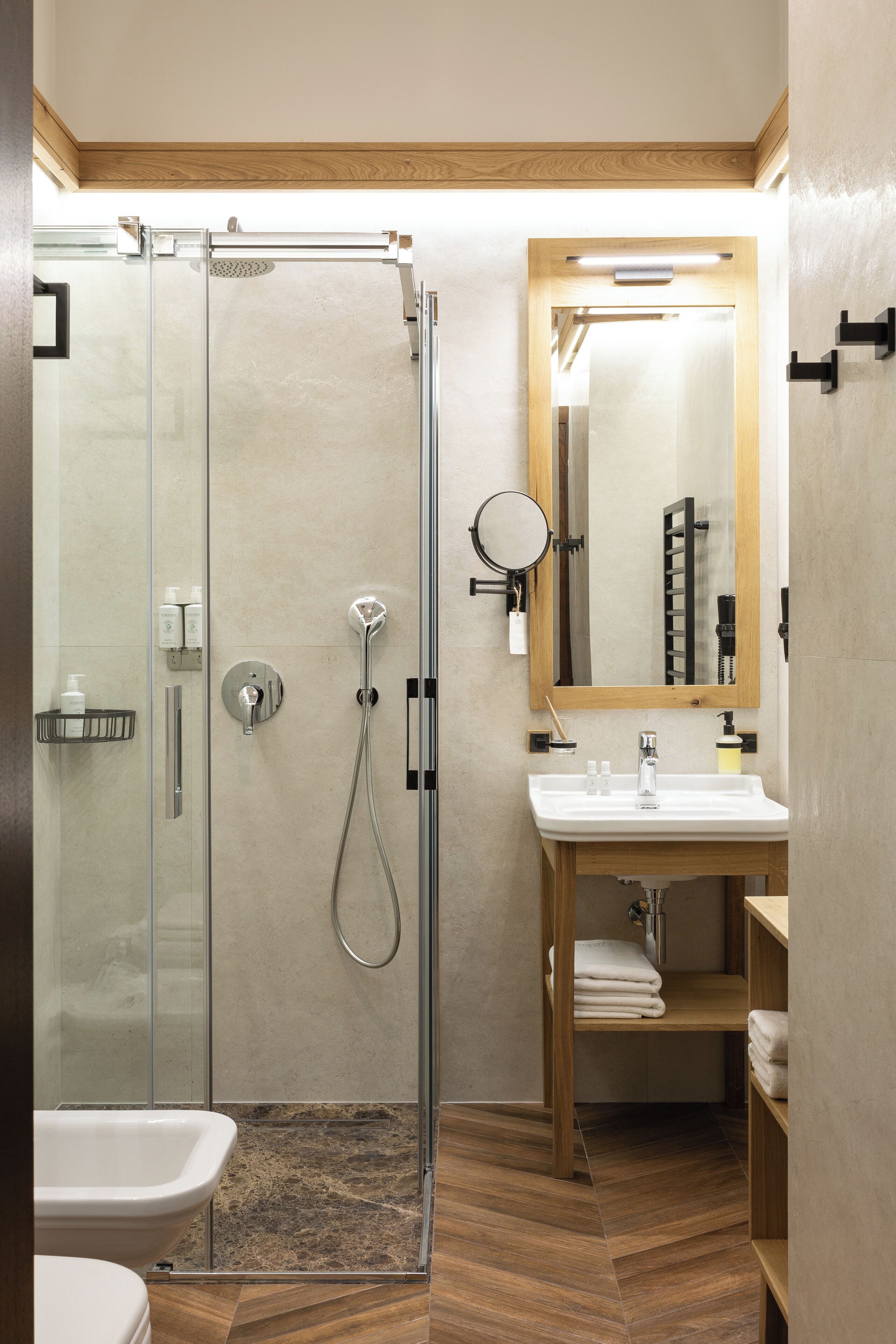 A modern bathroom with a glass-enclosed shower, a wooden vanity with a mirror, and a white sink.