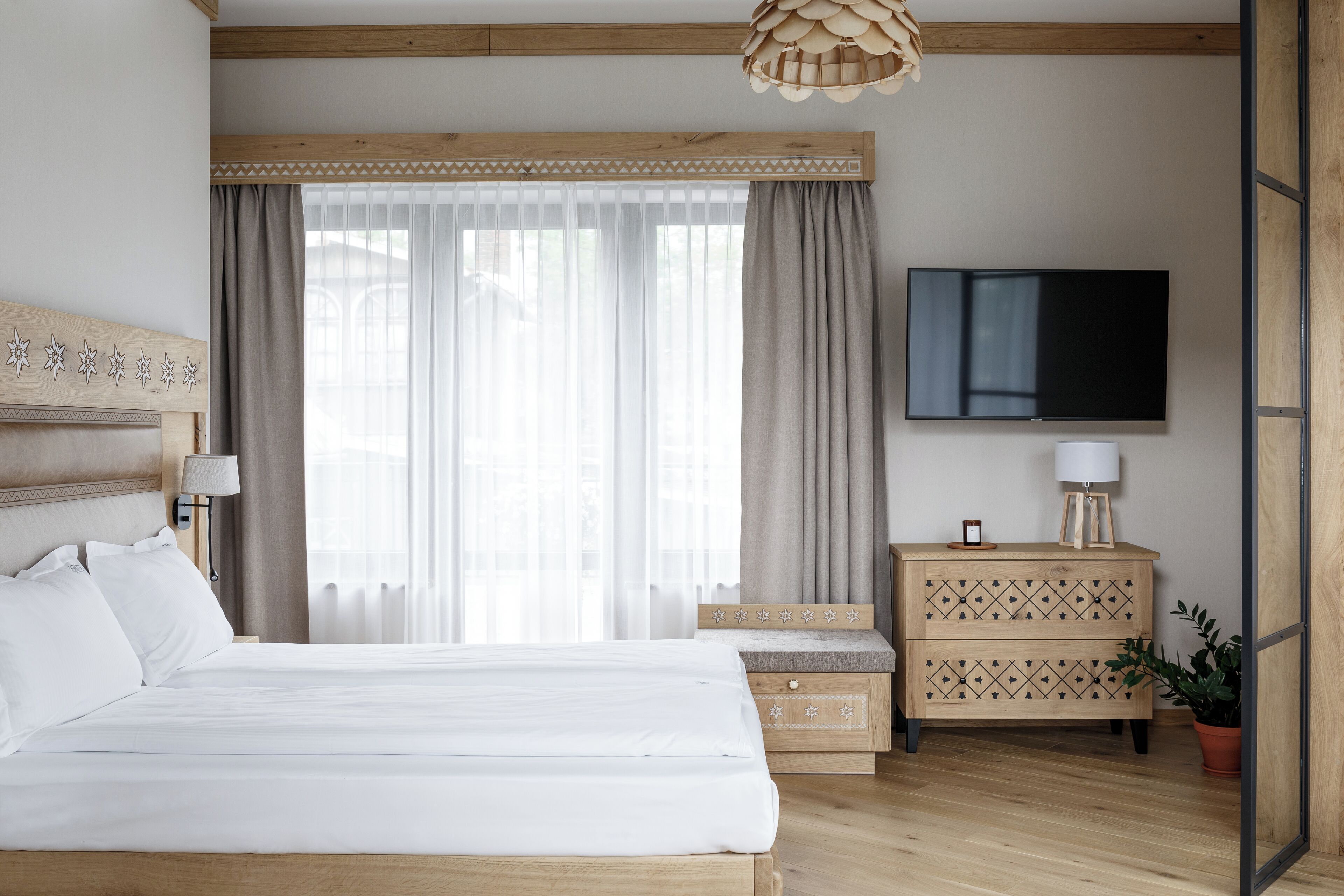A neatly arranged hotel room with a large bed, a television, a wooden dresser, and a potted plant.