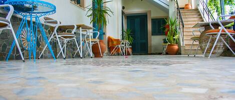 A courtyard with a tiled floor, outdoor seating with chairs and a table, potted plants, and a staircase.